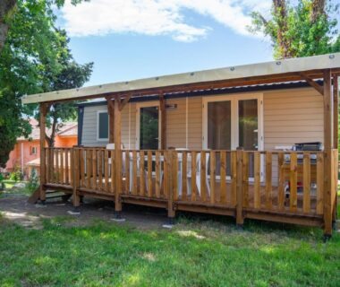 Mobil home avec terrasse en bois dans un espace herbeux au Camping Parc Bellevue