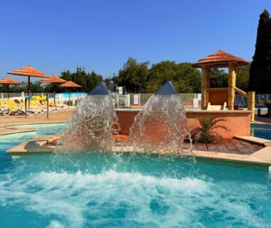 Piscine extérieure avec jets d'eau et parasols au Camping Parc Bellevue