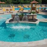 Piscine extérieure avec jets d'eau et transats au Camping Parc Bellevue Maeva