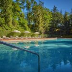 Piscine extérieure avec transats entourée d'arbres au Camping Parc des Roches
