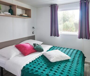 Chambre avec lit couverture verte et fenêtre au Camping Porte des Vosges