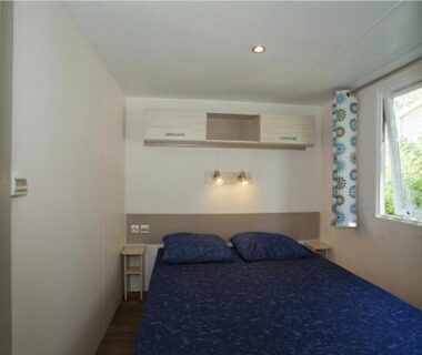 Chambre double avec lit bleu et fenêtre dans le camping RCN La Bastide en Ardèche