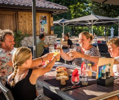 Terrasse extérieure avec famille levant leurs verres au Camping RCN La Bastide en Ardèche