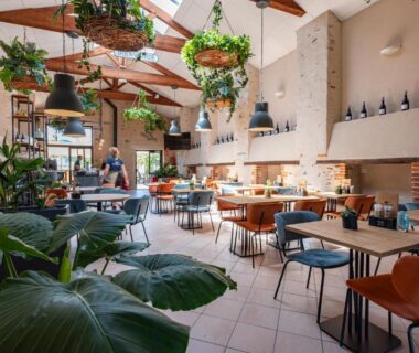 Salle de restaurant intérieure avec plantes suspendues et tables du Camping RCN La Ferme du Latois