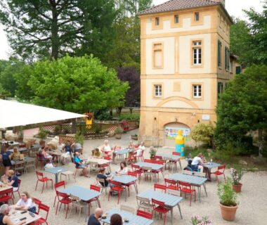 Terrasse ombragée avec tables et parasols dans la cour au Camping RCN Le Moulin de la Pique