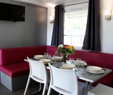 Coin repas intérieur avec banquette rouge et table dressée du Camping Resort Les Champs Blancs