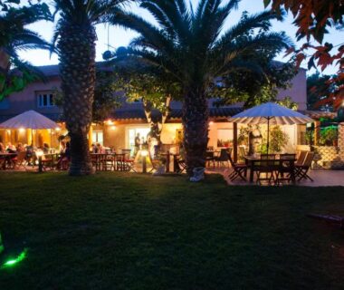Terrasse extérieure éclairée avec palmiers et parasols au Camping Resort Les Champs Blancs