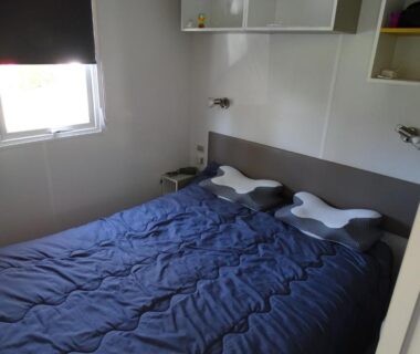 Chambre avec lit double et couette bleue dans le mobil-home climatisé du Camping Rivages des Landes