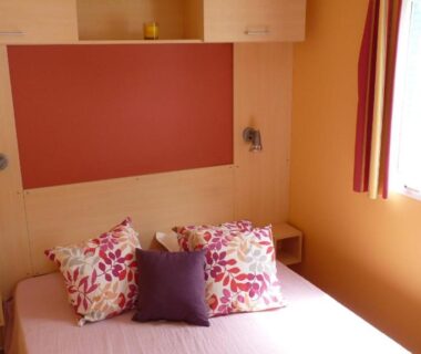 Chambre intérieure avec lit, coussins et fenêtre dans le Camping Sable d'Or 3 chambres