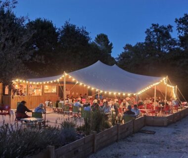 Esplanade sous chapiteau avec tables et guirlandes éclairées au Camping Saint Laurent