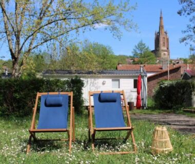 Pelouse avec deux chiliennes face aux mobil-homes et clocher au Camping Sud AVEYRON dans le Rougier