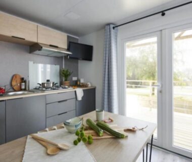 Intérieur de mobil-home avec kitchenette et table donnant sur terrasse au Camping Sud AVEYRON dans le Rougier