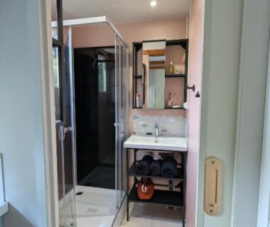 Salle de bain avec cabine de douche, lavabo et miroir dans l'hébergement du Camping TIKITI
