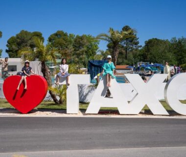 Entrée avec panneau I cœur TAXO et personnes assises au Camping Taxo Les Pins