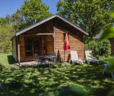 Terrasse herbeuse avec chaises et parasol devant chalet au camping Terre d'Armor