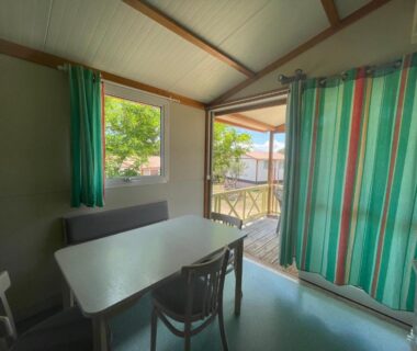 Intérieur d'un mobil-home avec table et chaises donnant sur terrasse au Camping Trinité