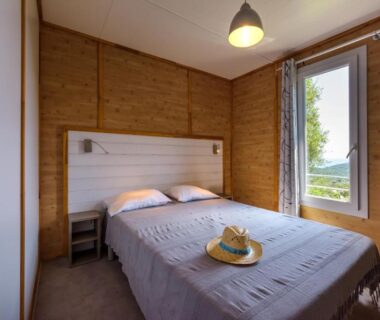 Chambre intérieure avec lit, fenêtre et chapeau posé sur le lit au Camping U Pirellu