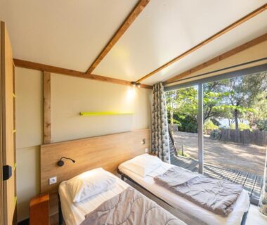 Chambre avec deux lits et baie vitrée donnant sur terrasse boisée au Camping Vigna Maggiore