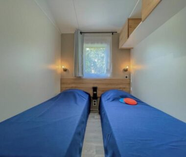 Intérieur de chambre avec deux lits simples et fenêtre au Camping de Brouël