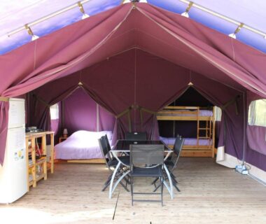 Intérieur de tente avec table chaises et lits superposés au Camping de Matour - ONLYCAMP