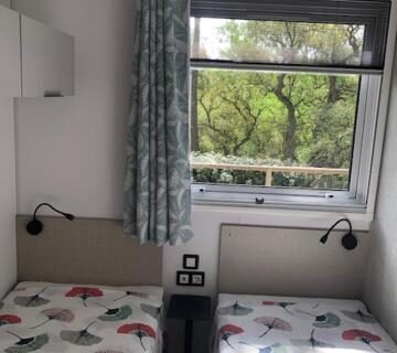 Chambre avec deux lits jumeaux et fenêtre sur la végétation au Camping de Parpaillon