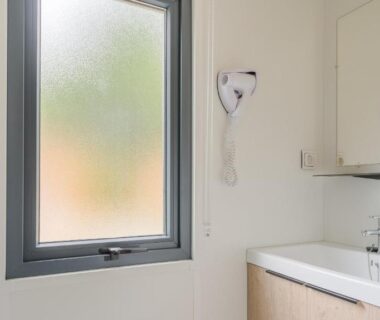 Salle de bain avec lavabo miroir fenêtre et sèche-cheveux au Camping de Saverne