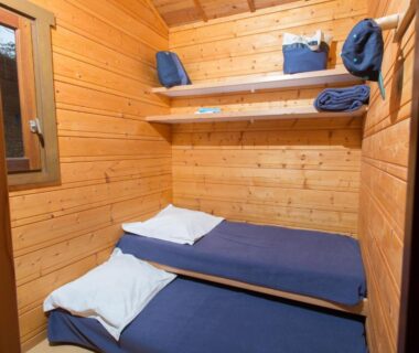 Cabine en bois avec lits superposés et étagères avec serviettes pliées au Camping de Tauves