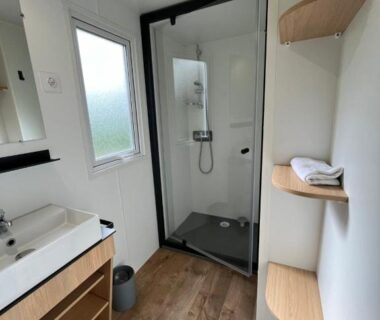Salle de bain avec douche vitrée et lavabo au Camping de Tauves
