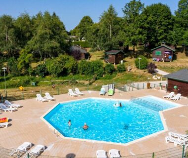Piscine extérieure entourée de transats et de chalets en bois au Camping de Tauves