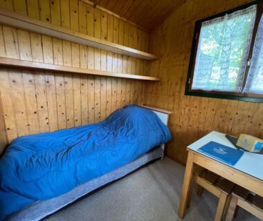 Intérieur de chalet avec lit simple, bureau et fenêtre au Camping de Tauves