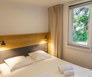 Chambre avec lit double serviettes et fenêtre sur végétation au Camping de l'Orangerie de Lanniron
