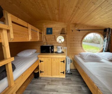 Intérieur de cabine en bois avec lits superposés et hublot au Camping de la Bageasse