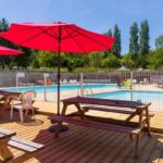Terrasse avec parasols rouges et piscine au Camping de la Baie de Térénez