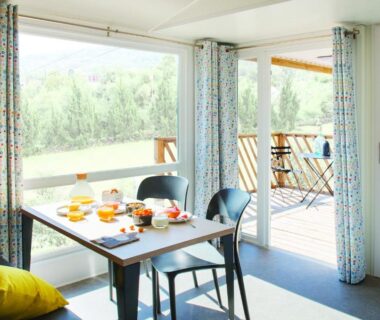 Coin repas intérieur et terrasse en bois donnant sur la verdure au Camping de la Baie de Térénez