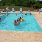 Piscine extérieure avec baigneurs et transats au Camping de la Pelouse