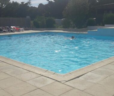 Piscine extérieure avec baigneurs et transats au Camping de la Rive