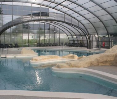 Piscine couverte sous dôme transparent avec aménagement rocheux au Camping des Roses