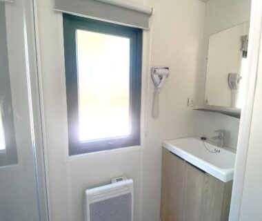 Salle de bains avec lavabo miroir et sèche-cheveux dans l'hébergement du Camping du Chêne