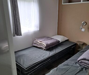 Chambre avec deux lits simples et fenêtre dans l'hébergement du Camping du Domaine de la Forge