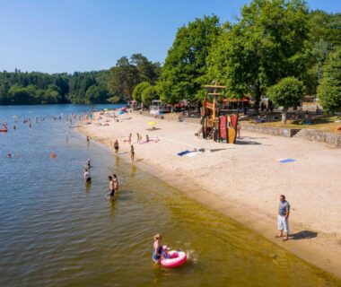 Plage de sable avec baigneurs et aire de jeux au Camping du Lac