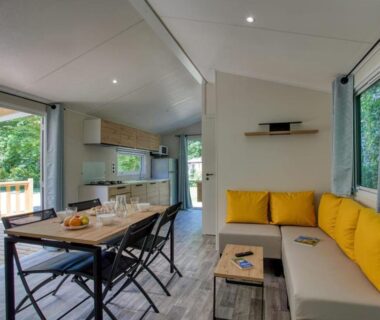 Salon ouvert avec banquette jaune et table à manger donnant sur terrasse au Camping du Lac de Grolejac