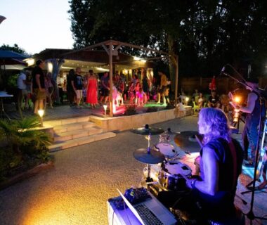 Scène extérieure avec batteur et public en soirée au Camping du Lac de Grolejac