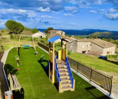 Aire de jeux sur pelouse avec toboggan et panorama des collines du Camping du Vignal