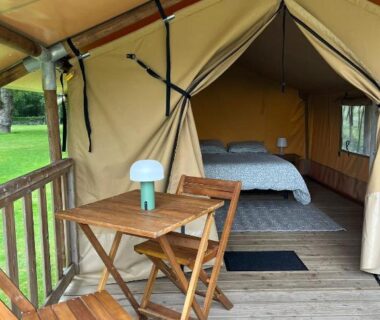 Terrasse de tente avec table en bois et lit visible au Camping du pont d’Oust