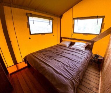 Intérieur de lodge avec lit double et fenêtres au Camping et Lodges de Coucouzac