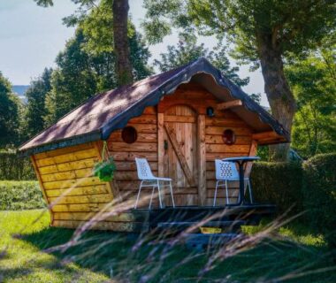 Cabane en bois sur pelouse entourée d'arbres au Camping l'Estela sur le GR70