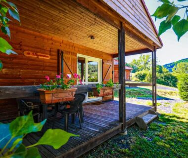 Terrasse couverte d'un chalet en bois avec table et jardinières au Camping l'Estela sur le GR70
