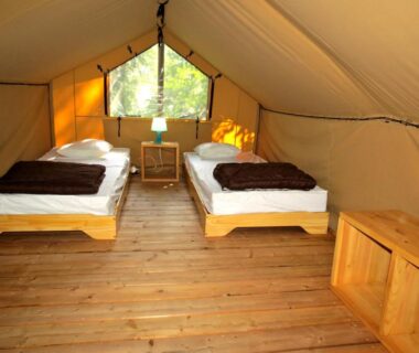 Intérieur de tente aménagée avec deux lits et plancher en bois dans le Camping l'Hirondelle Drôme