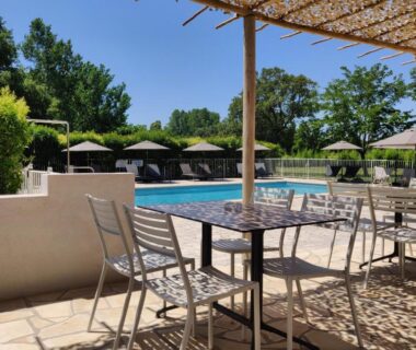 Terrasse ombragée avec table et chaises et piscine en arrière plan au Camping l'Oso