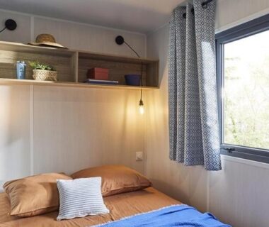 Chambre avec lit, étagères et fenêtre dans le mobil-home du Camping l'Oso